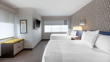 A hotel room with two beds, a desk, a TV, and a window with blinds.