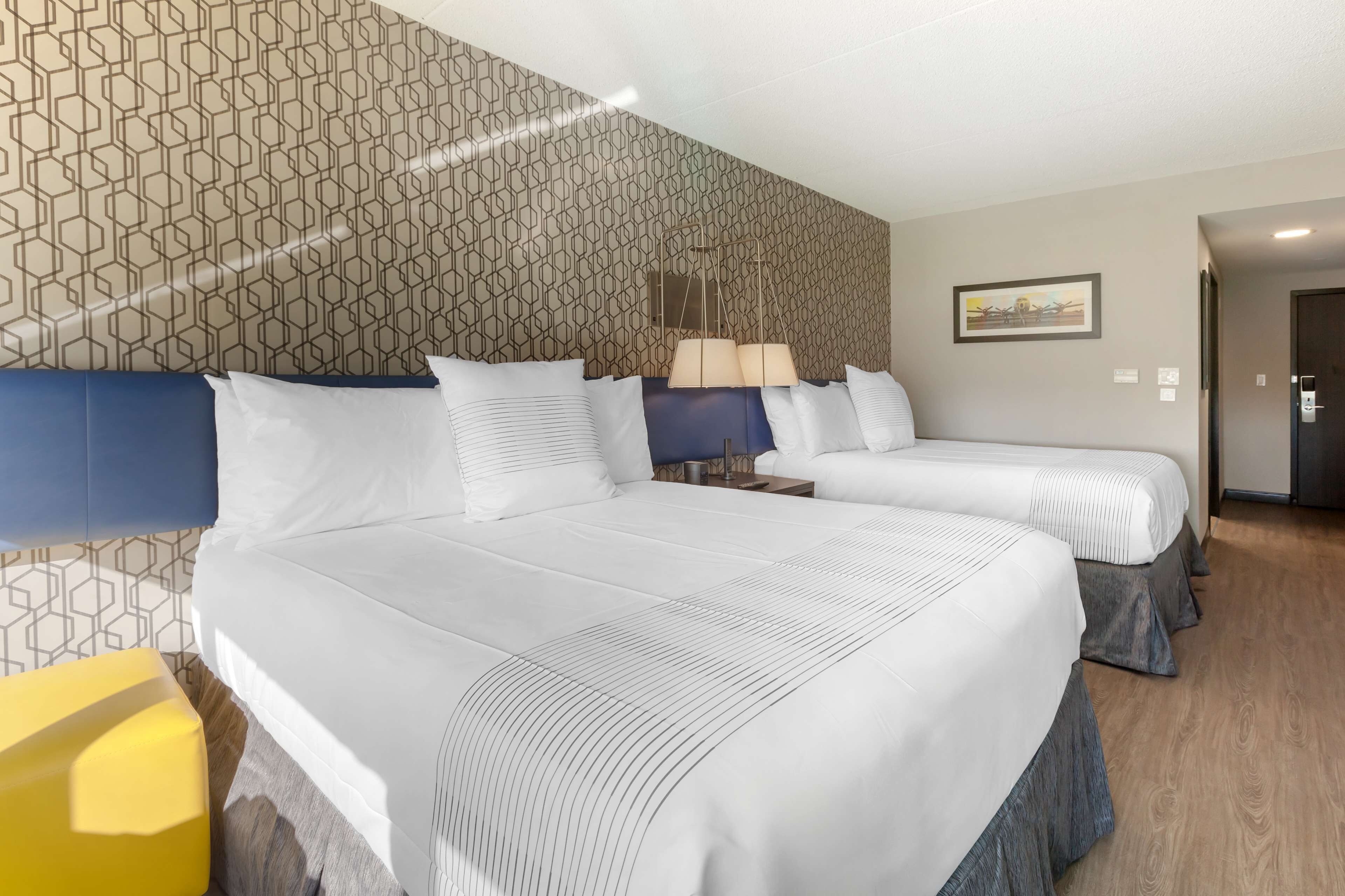 A hotel room with two beds, a patterned wall, a painting, and a wooden floor.