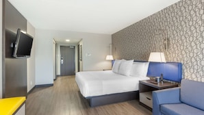 Una habitación de hotel con cama, mesitas de noche, televisor y un papel tapiz decorado.
