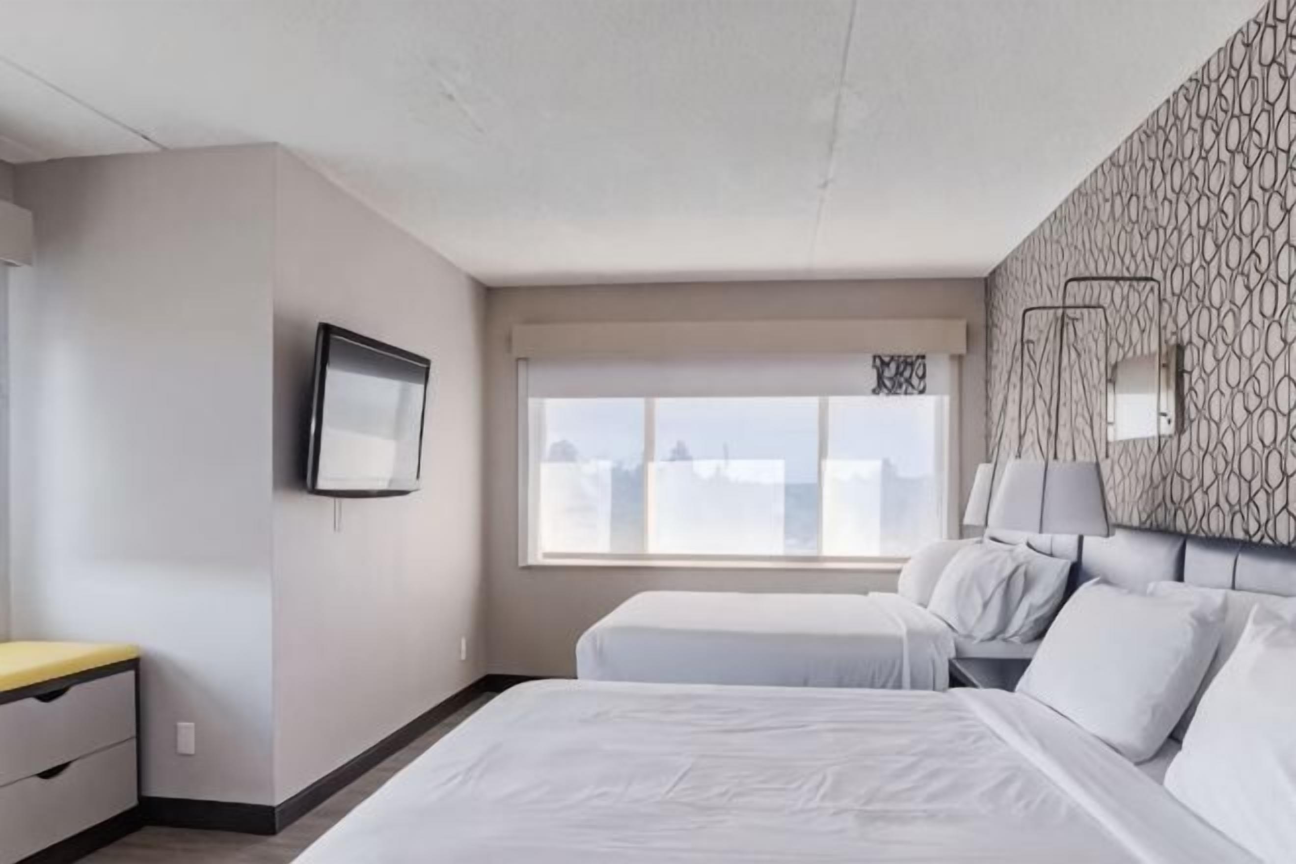 Une chambre d’hôtel avec un lit, des tables de chevet, une télévision, une fenêtre donnant sur un paysage agréable et un mur décoré d’un motif.