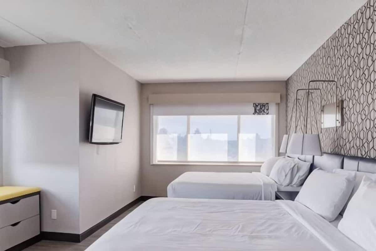 A hotel room with a bed, bedside tables, a TV, a window with a view, and a patterned wall.