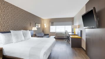 A hotel room with a large bed, a desk, a chair, a TV, and a window with a view.