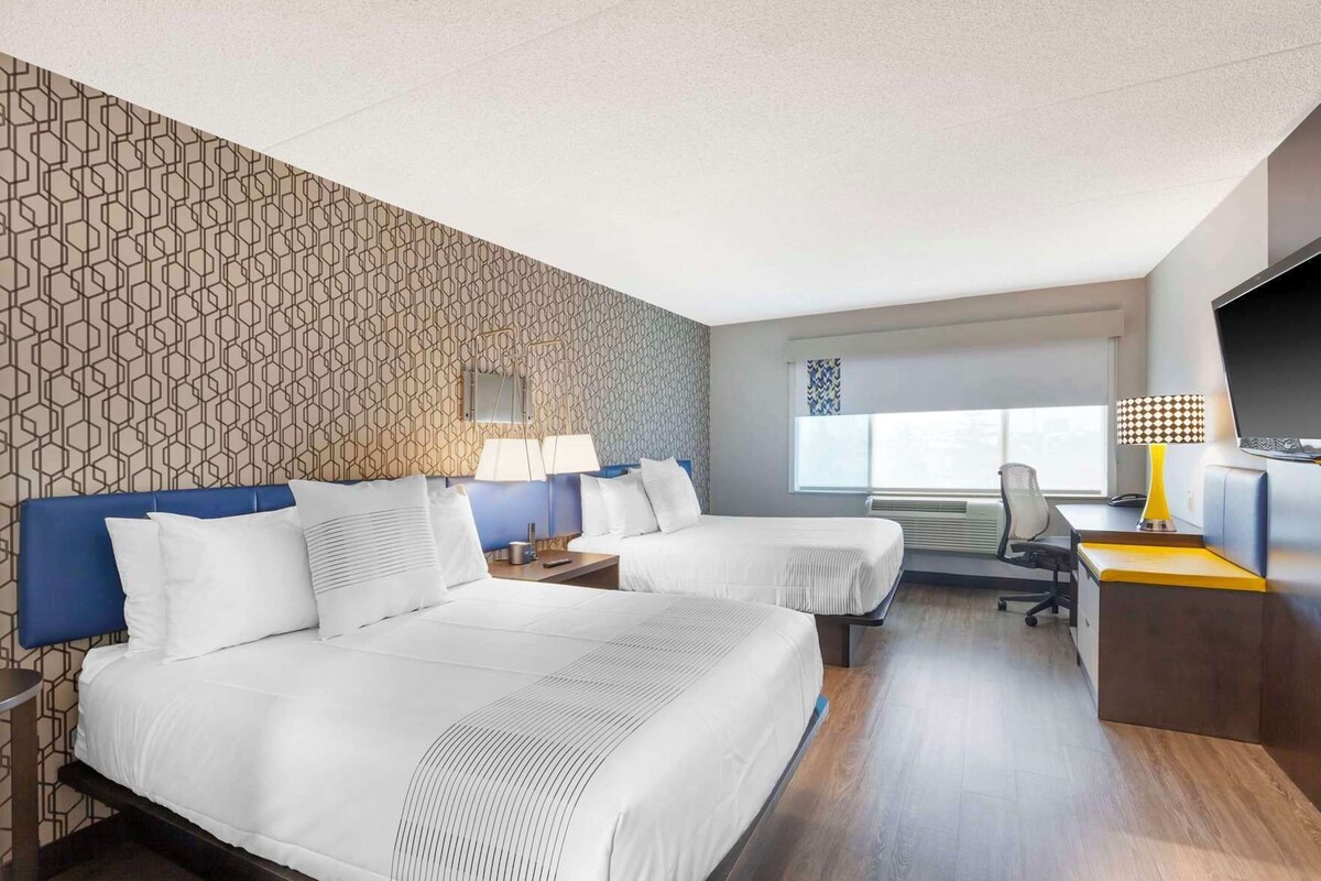 A hotel room with two beds, a desk, a chair, a TV, and a window with blinds.