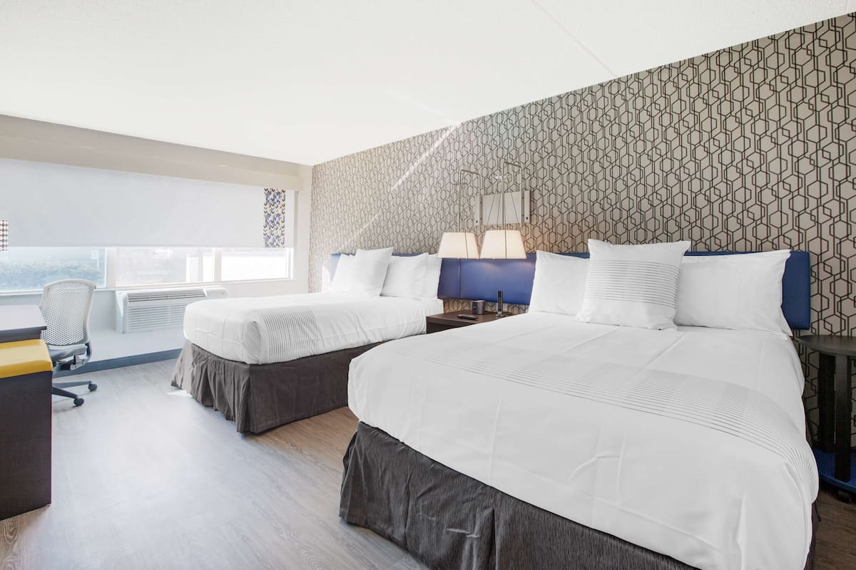 Una habitación de hotel con dos camas, un escritorio y un ventanal.