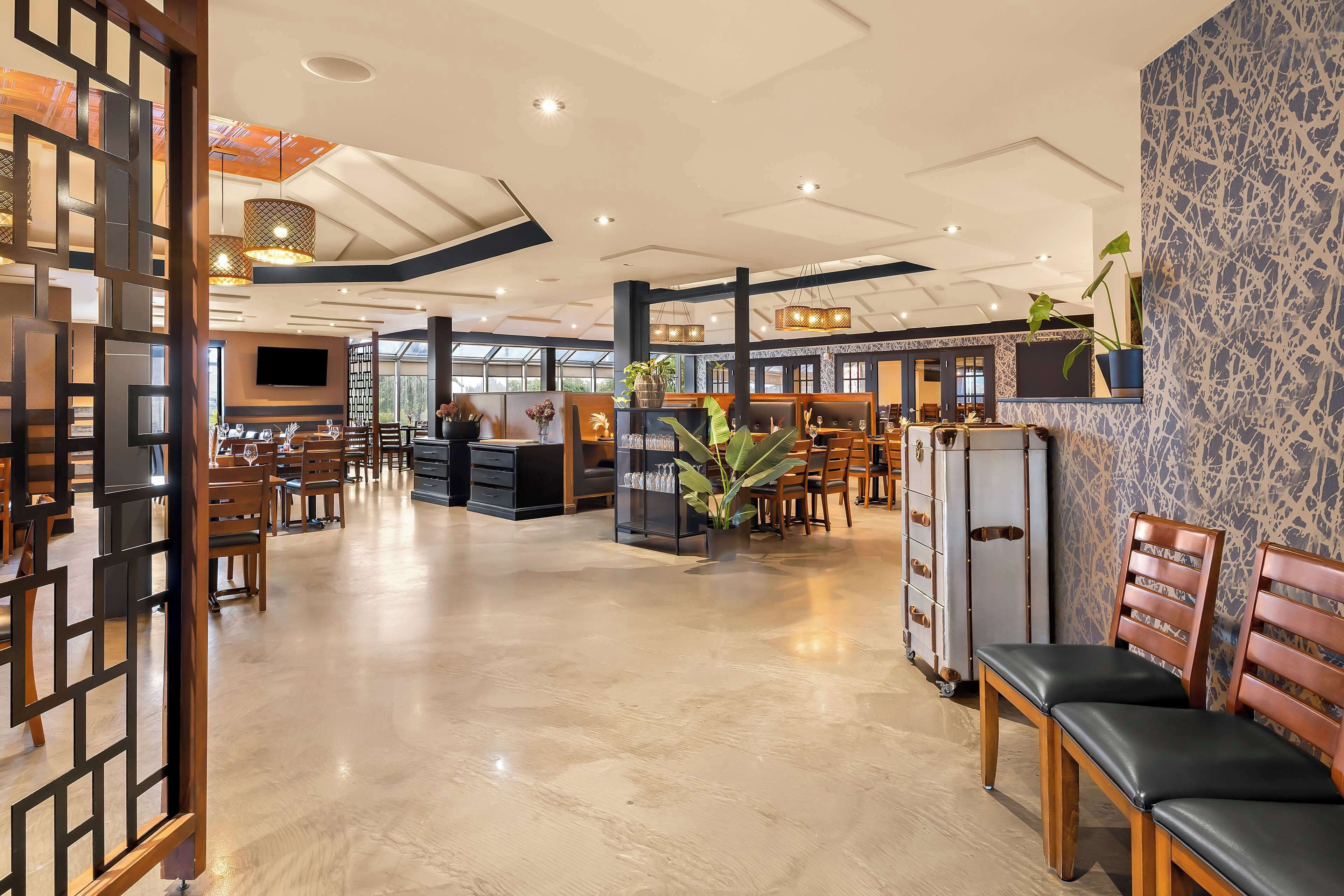 A spacious hotel lobby with wooden furniture, a reception desk, and a large plant.