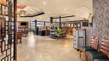 A spacious hotel lobby with wooden furniture, a reception desk, and a large plant.