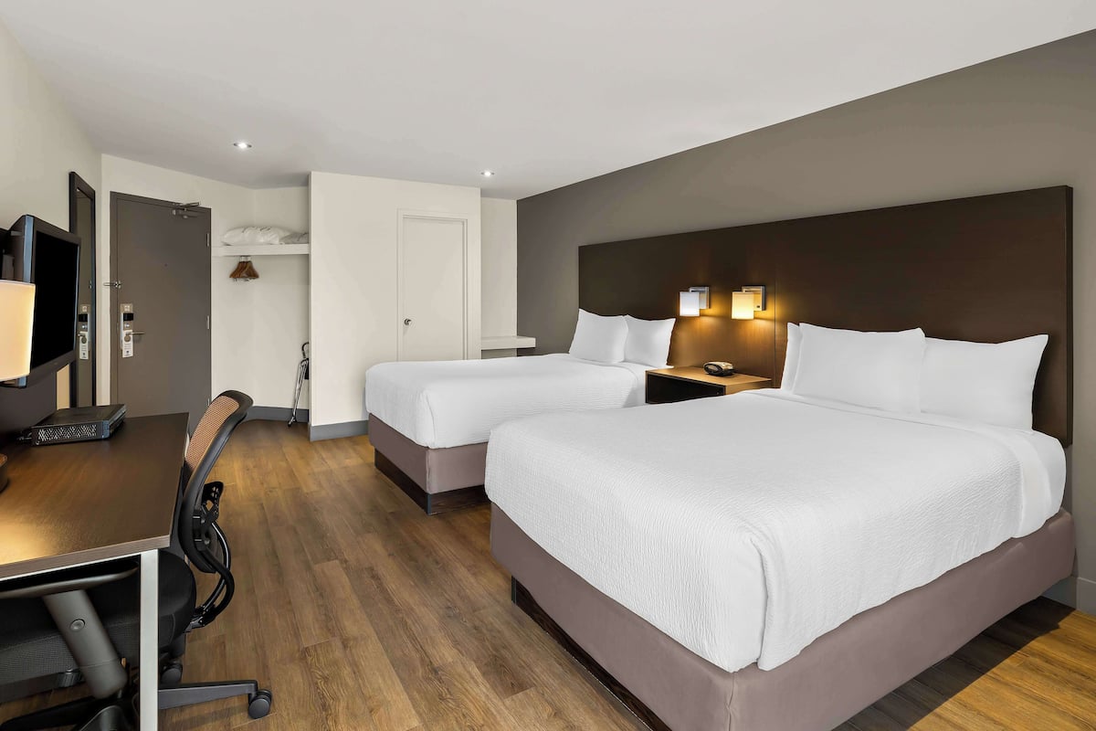 Ein Hotelzimmer mit zwei Betten, einem Schreibtisch, einem Stuhl, einem Fernseher und einer Wandleuchte.