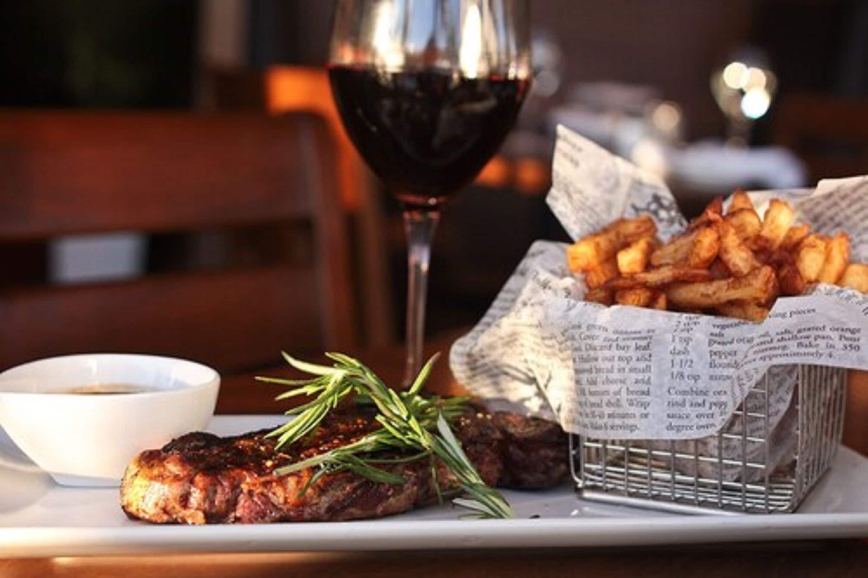 A plate with grilled meat, a glass of red wine, a basket of fries, and a small bowl of sauce.