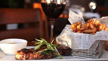 A plate with grilled meat, a glass of red wine, a basket of fries, and a small bowl of sauce.