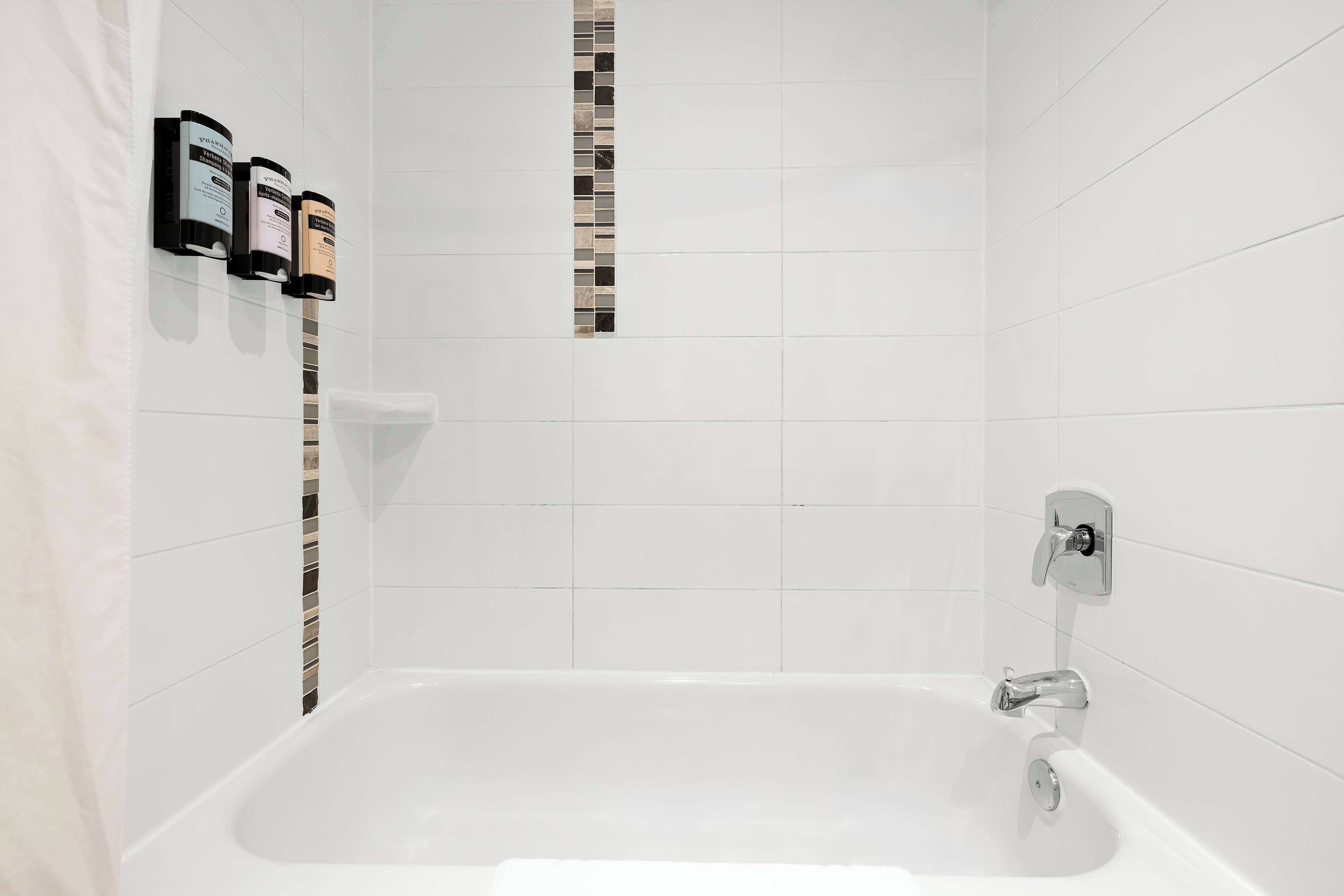 A modern bathroom with a white bathtub, a vertical strip of mosaic tiles, and three toiletries dispensers mounted on the wall.