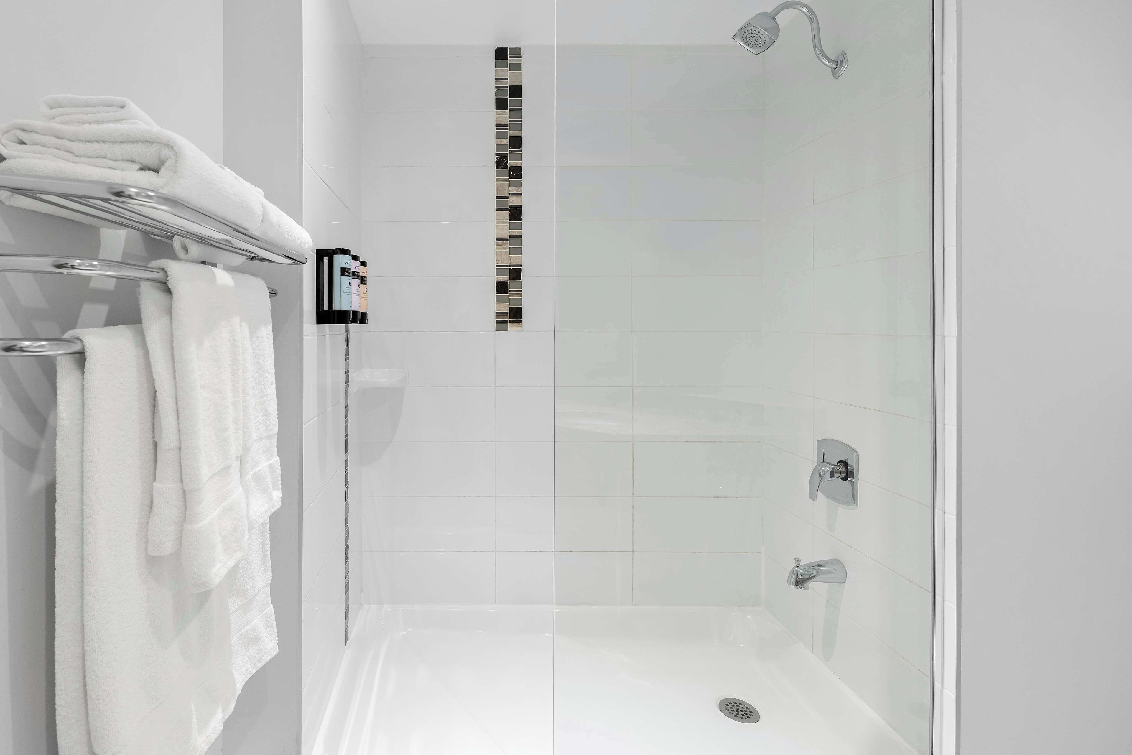 Un baño moderno con ducha de vidrio, azulejos blancos y toallas dobladas ordenadamente en un perchero.