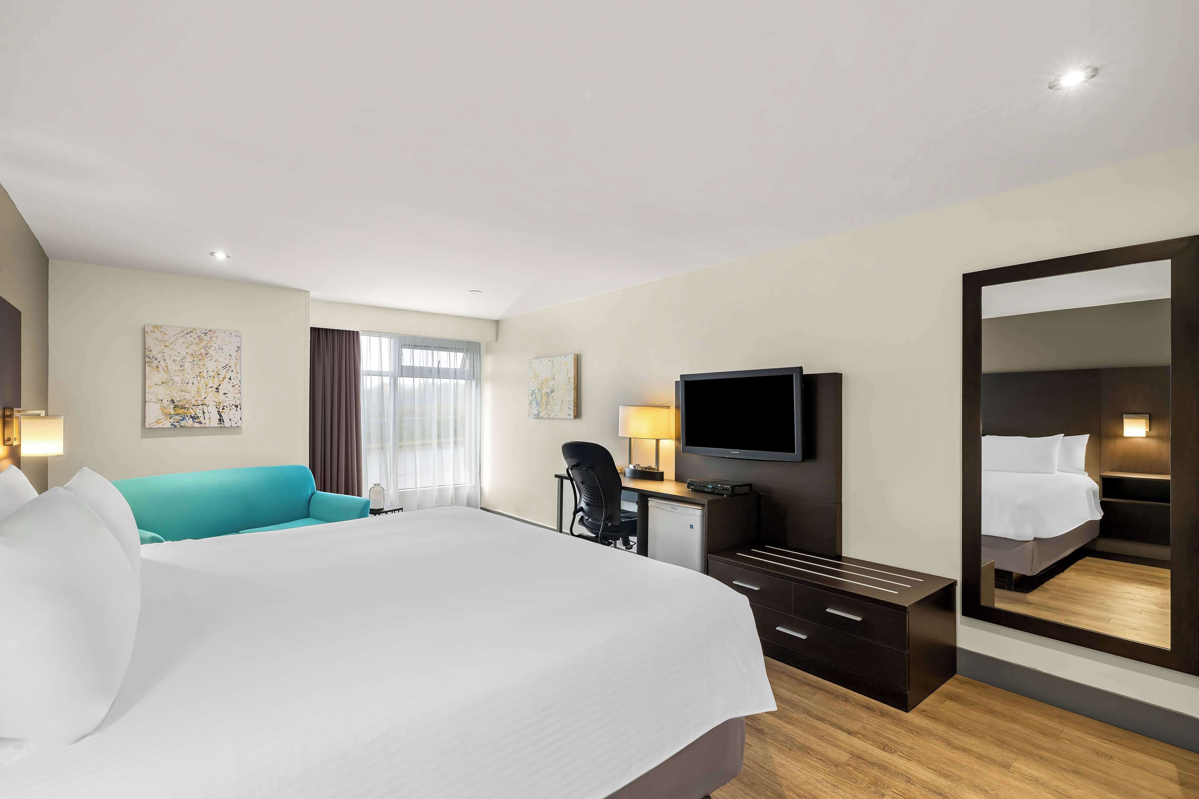 A hotel room with a large bed, a desk with a chair, a television, and a mirror.