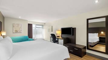 A hotel room with a large bed, a desk with a chair, a television, and a mirror.