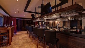 Zona de bar con una barra larga, varios taburetes y una estantería para vinos.