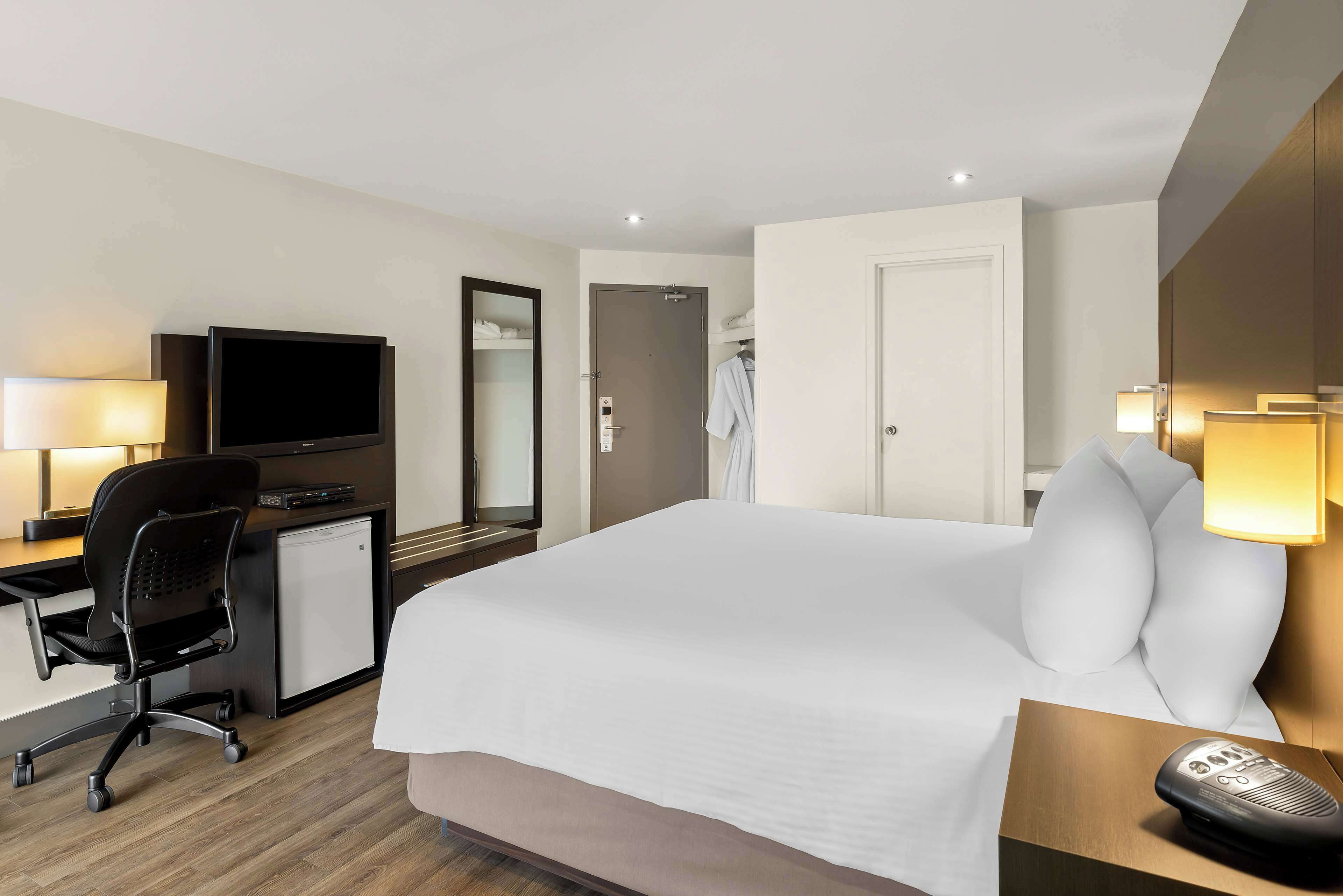 A hotel room with a bed, desk, chair, television, and a shower area.
