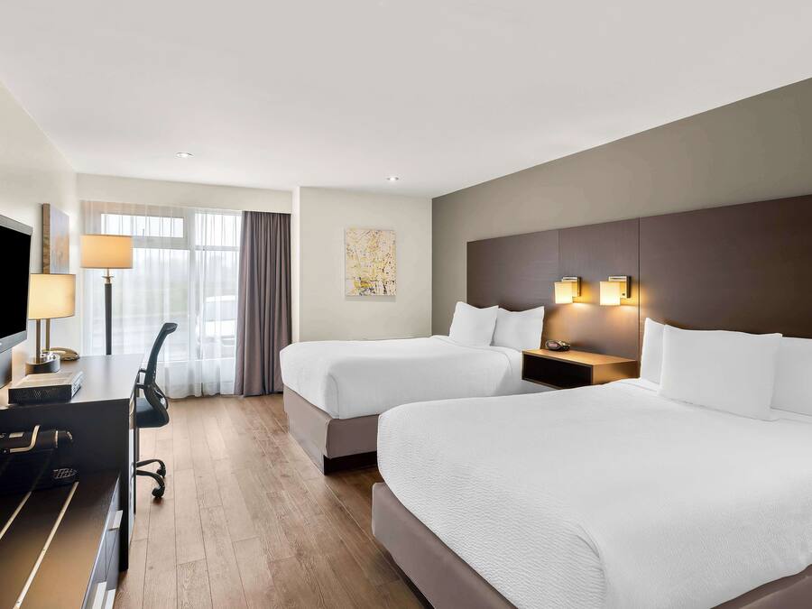 Habitación de hotel con dos camas, un escritorio con televisor, una lámpara y un cuadro en la pared.