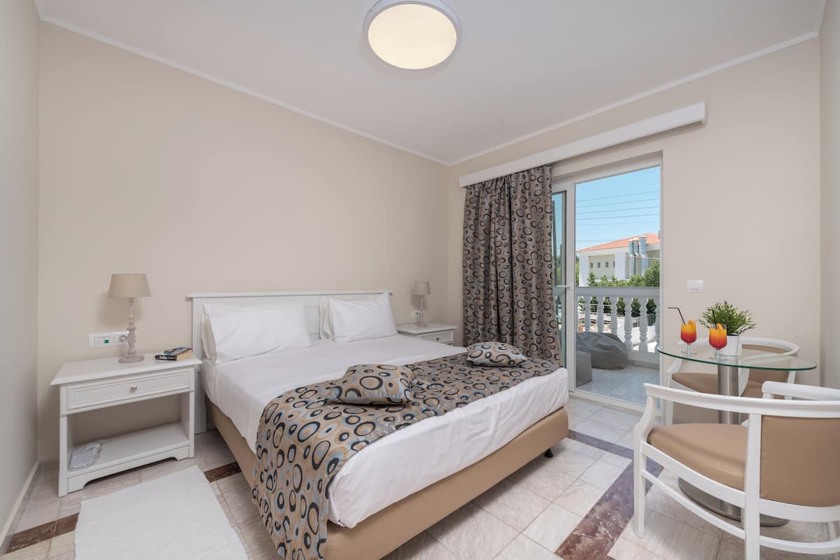 A hotel room with a bed, bedside tables, a small table with chairs, and a balcony with a view.