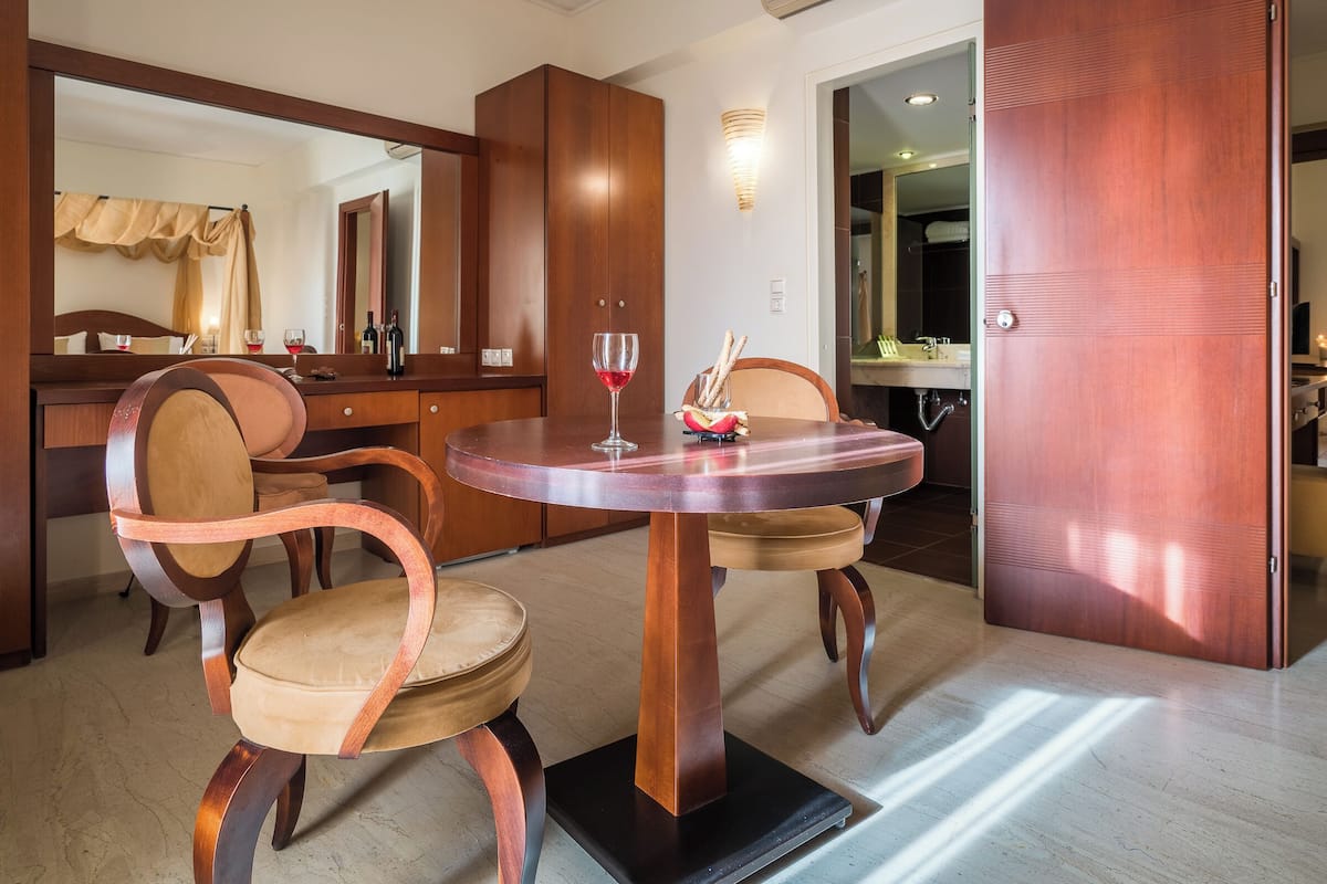 A hotel room with a wooden dining table, two chairs, a mirror, and a wardrobe.