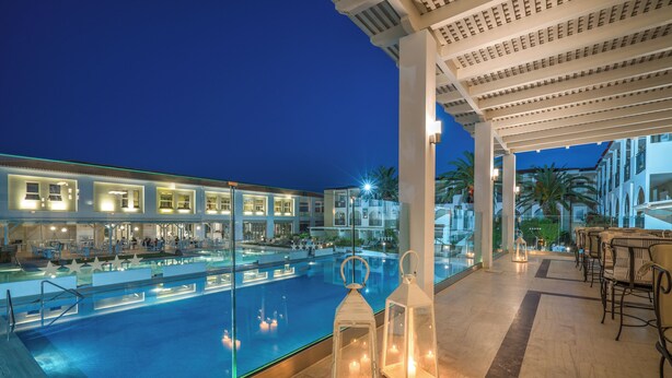 A poolside area with a glass barrier, outdoor seating, and a view of the pool. - Zante Park Resort & Spa, BW Premier Collection (Zakynthos)
