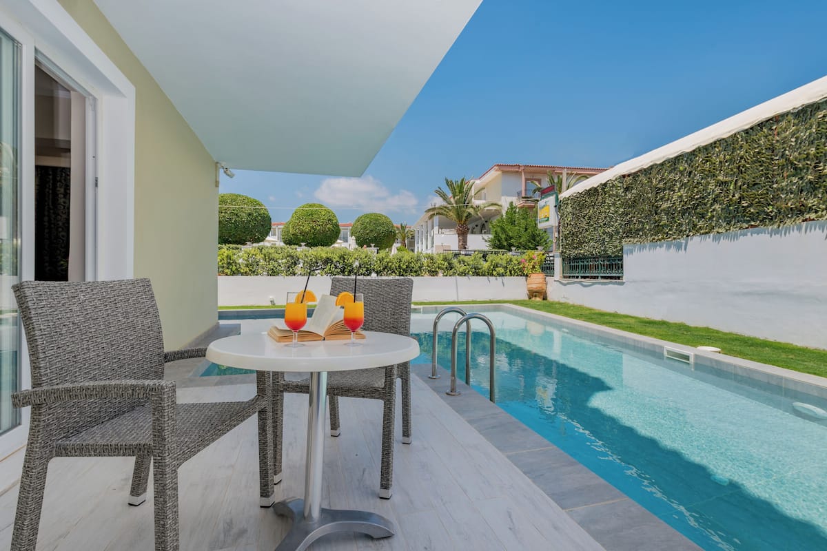 A poolside area with wicker chairs, a table with drinks, and a view of the pool and surrounding greenery.