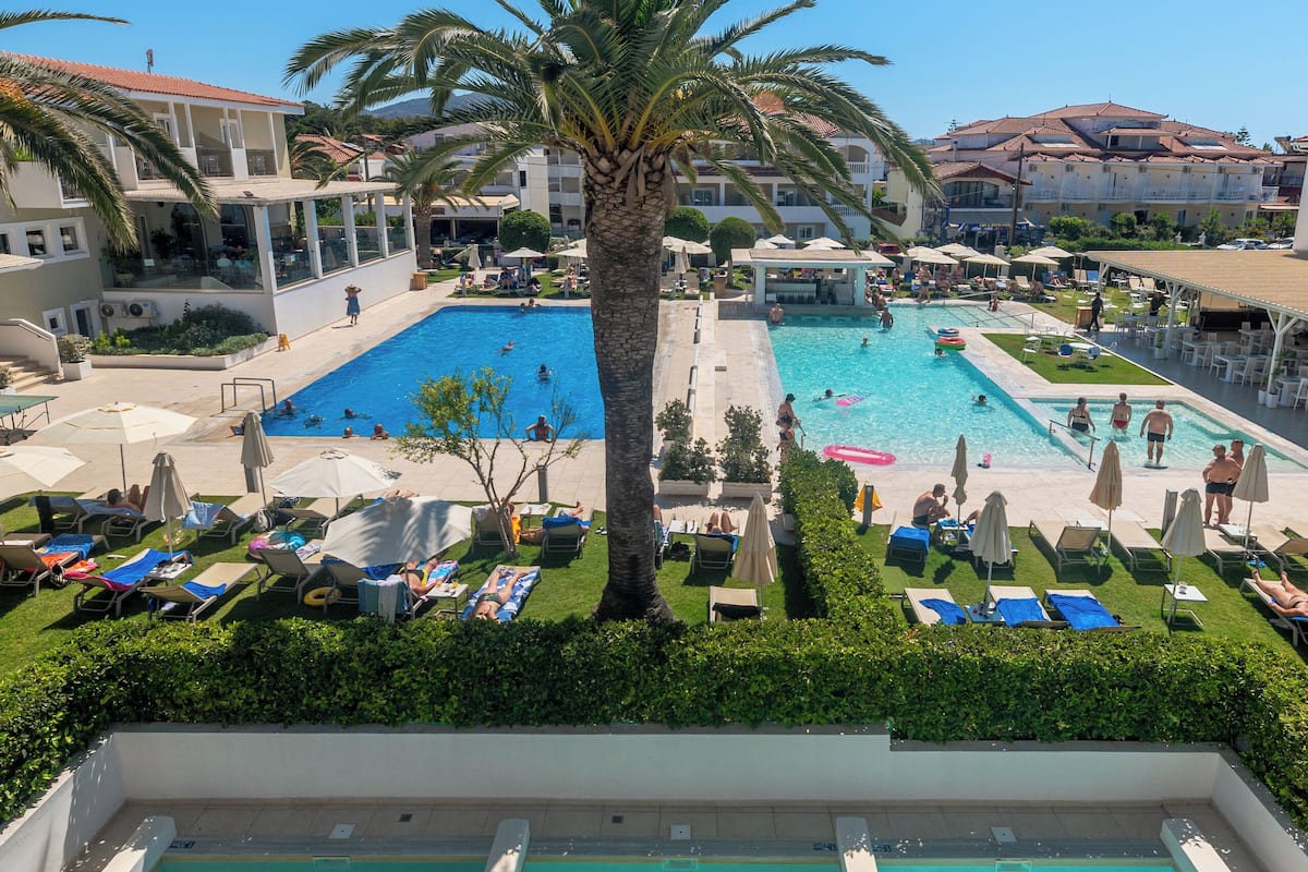 A resort pool area with multiple swimming pools, sun loungers, and palm trees.