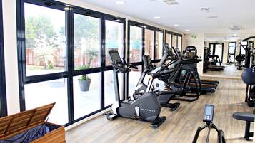 Un gimnasio con máquinas de cardio, una banca y grandes ventanales.