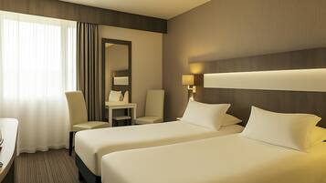 A hotel room with two beds, a desk, a chair, a mirror, and a lamp.