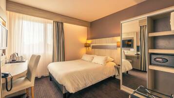 Una habitación de hotel con cama, escritorio, silla y espejo.