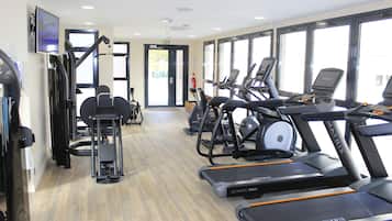 Een sportschool met loopbanden, gewichtstoestellen en een televisie aan de muur.