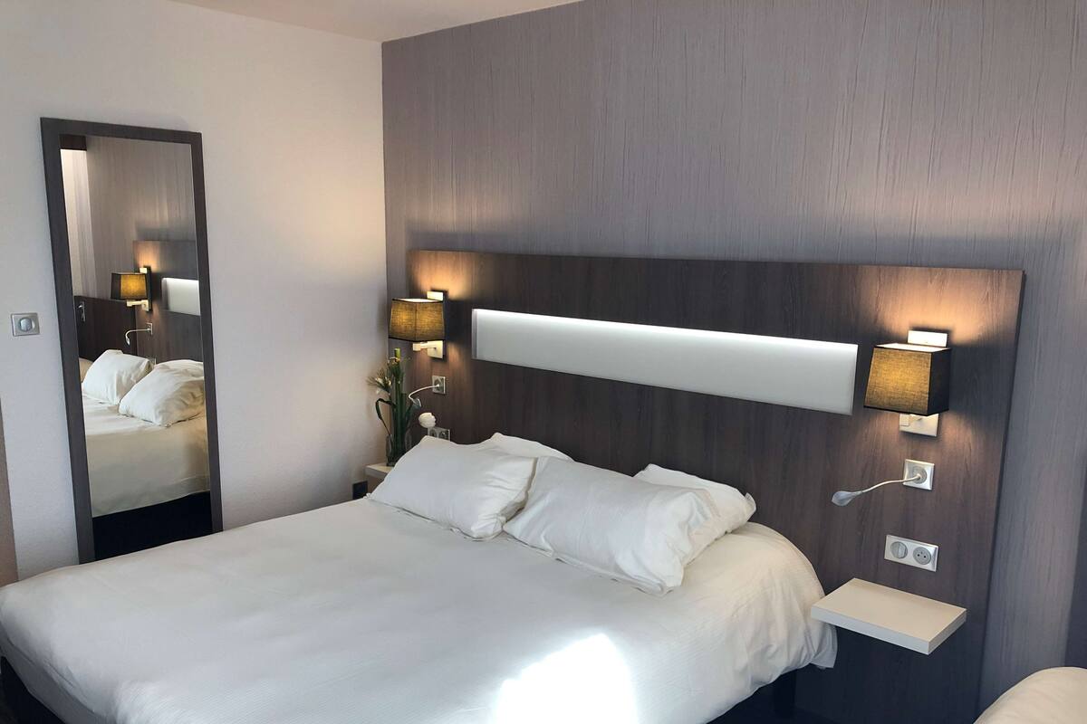 Ein modernes Hotelzimmer mit einem großen Bett, einem Nachttisch, einem Spiegel und Wandleuchten.