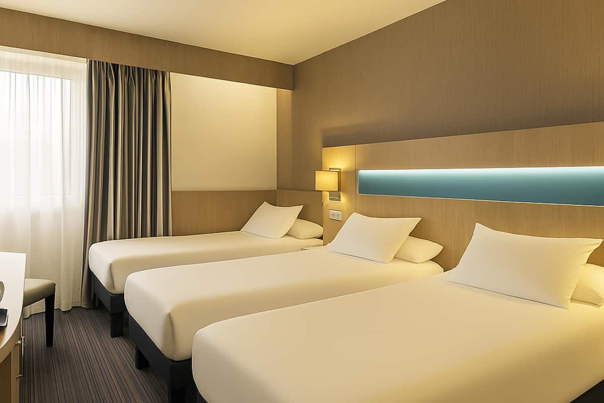 Ein Hotelzimmer mit drei Einzelbetten, einem Schreibtisch und einem Fenster mit Vorhängen.
