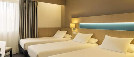 A hotel room with three single beds, a desk, and a window with curtains.