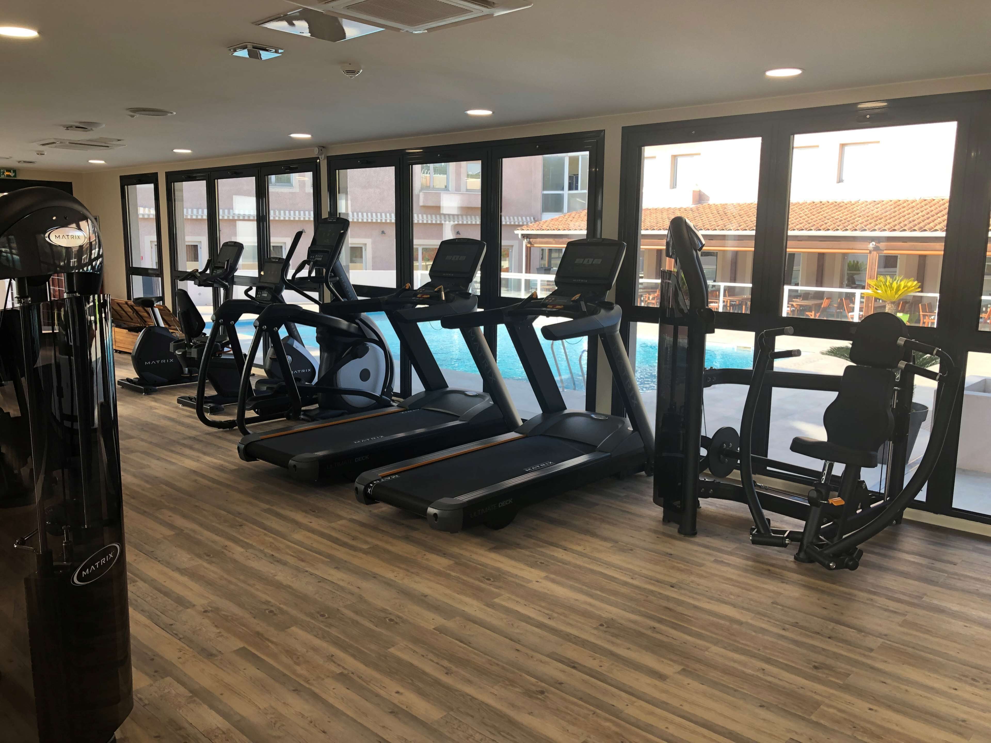 A gym with treadmills, exercise bikes, and a pool in the background.