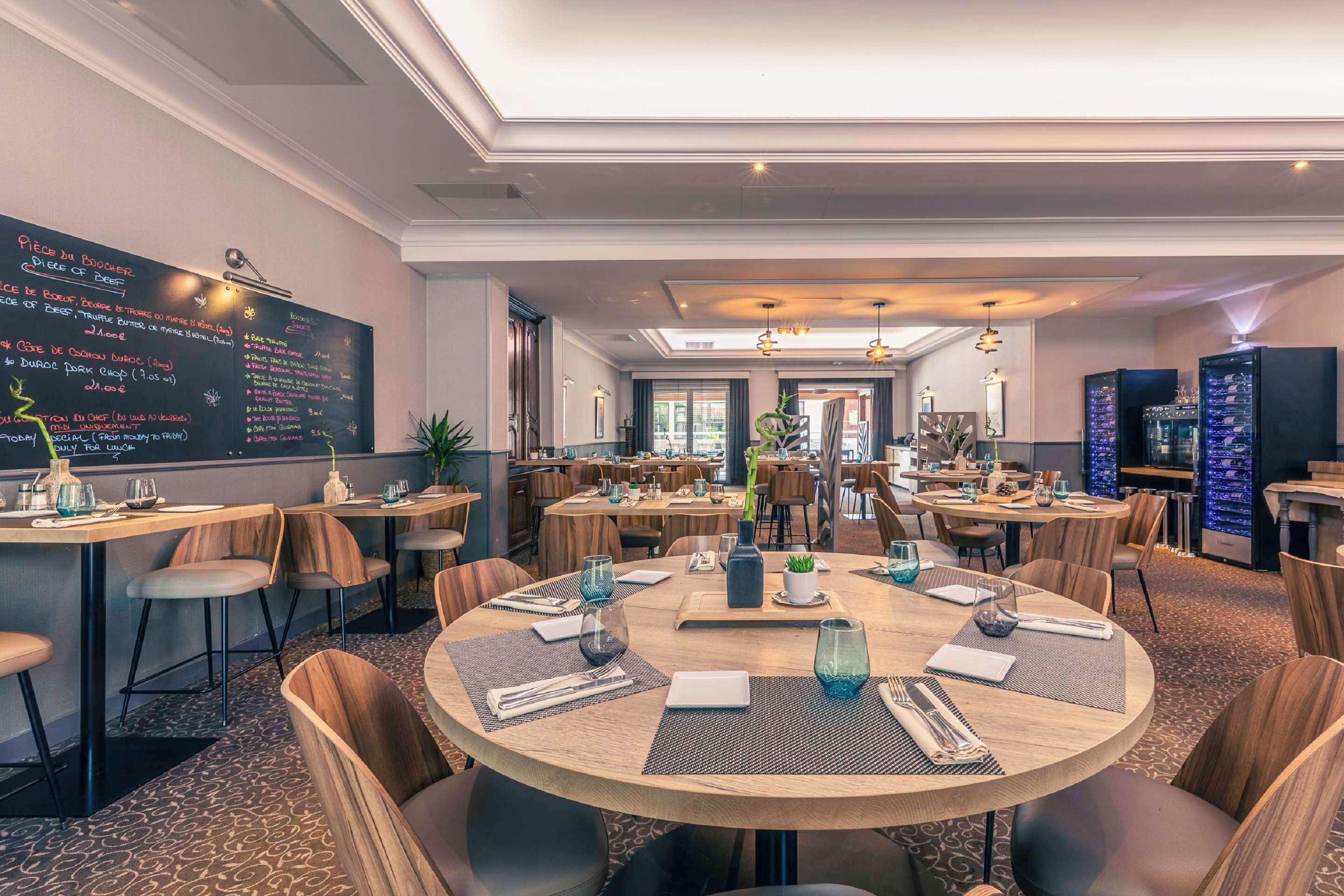 A restaurant with round tables, chairs, and a chalkboard menu.