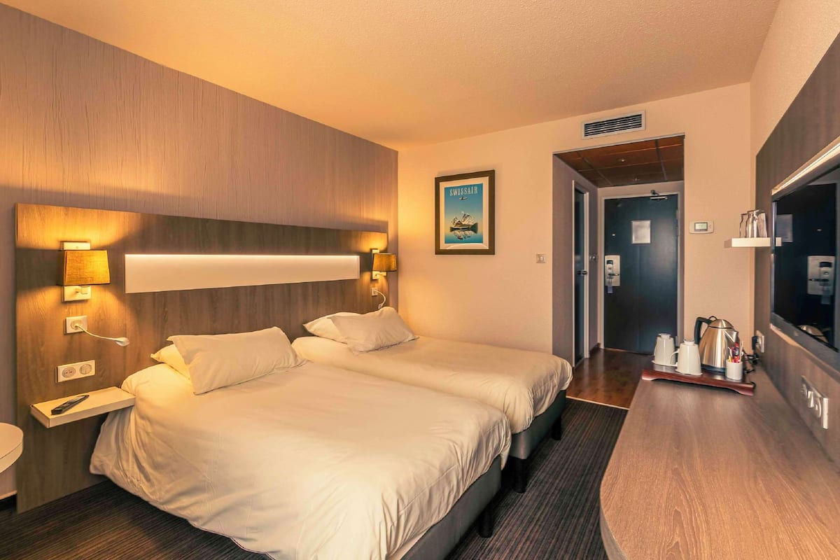 Ein Hotelzimmer mit zwei Betten, einem Nachttisch mit Lampe, einem Flachbildfernseher und einer Kaffeestation.