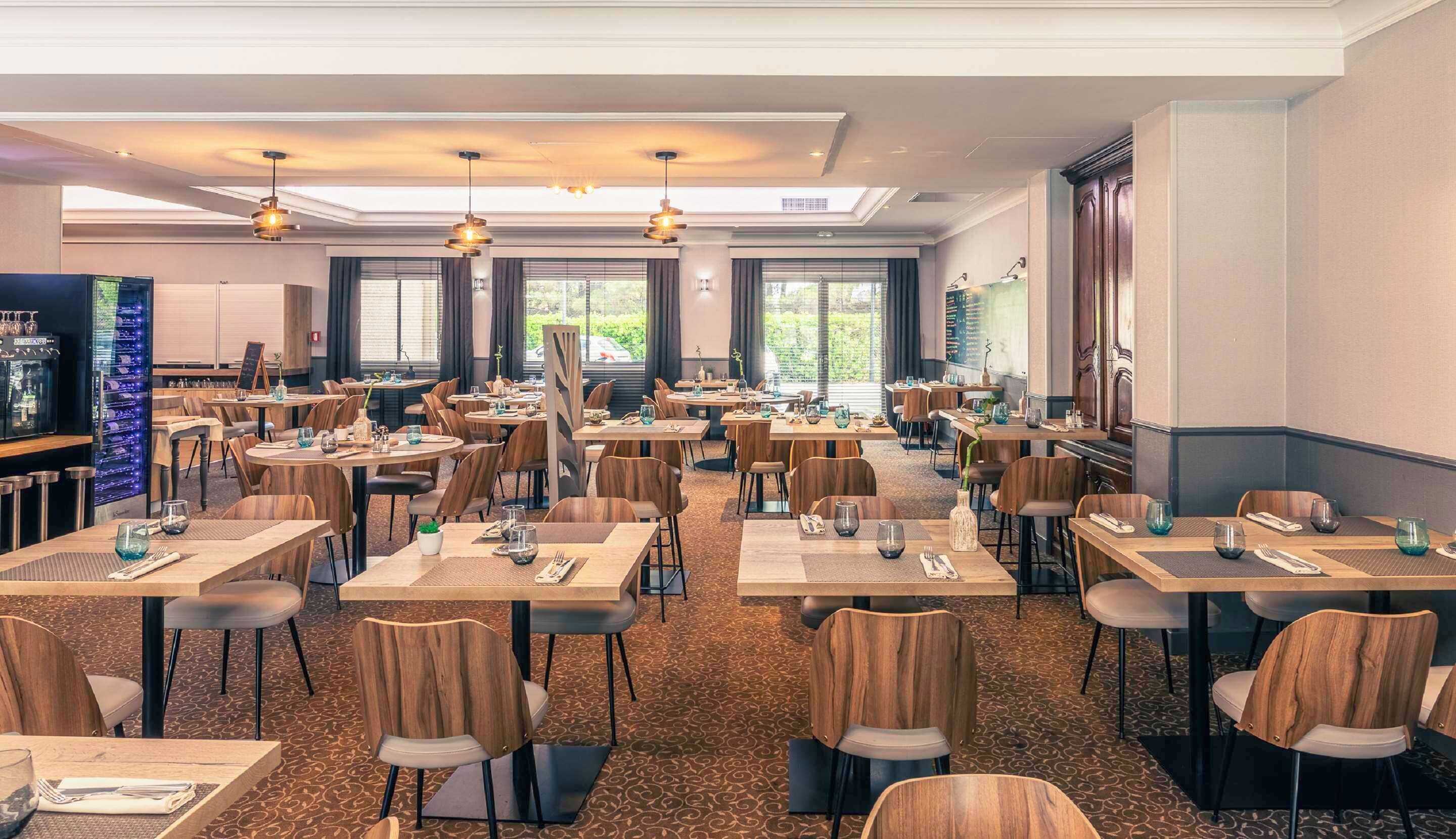 Un vaste espace dédié à la salle à manger, avec de nombreuses tables et chaises, de grandes fenêtres et un éclairage moderne suspendu au plafond.