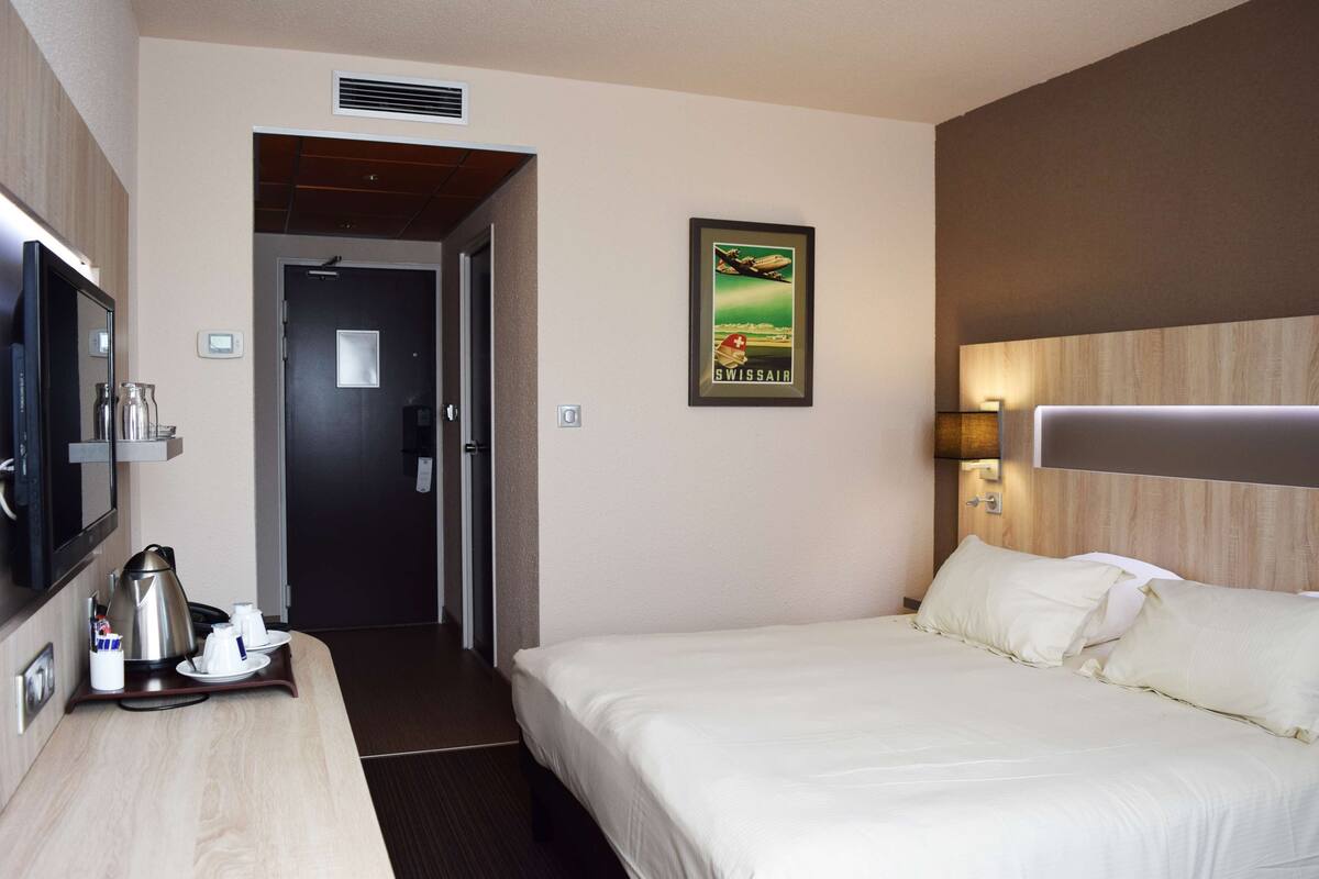 Ein Hotelzimmer mit einem Bett, einem Fernseher, einer Kaffeemaschine und einem gerahmten Bild an der Wand.