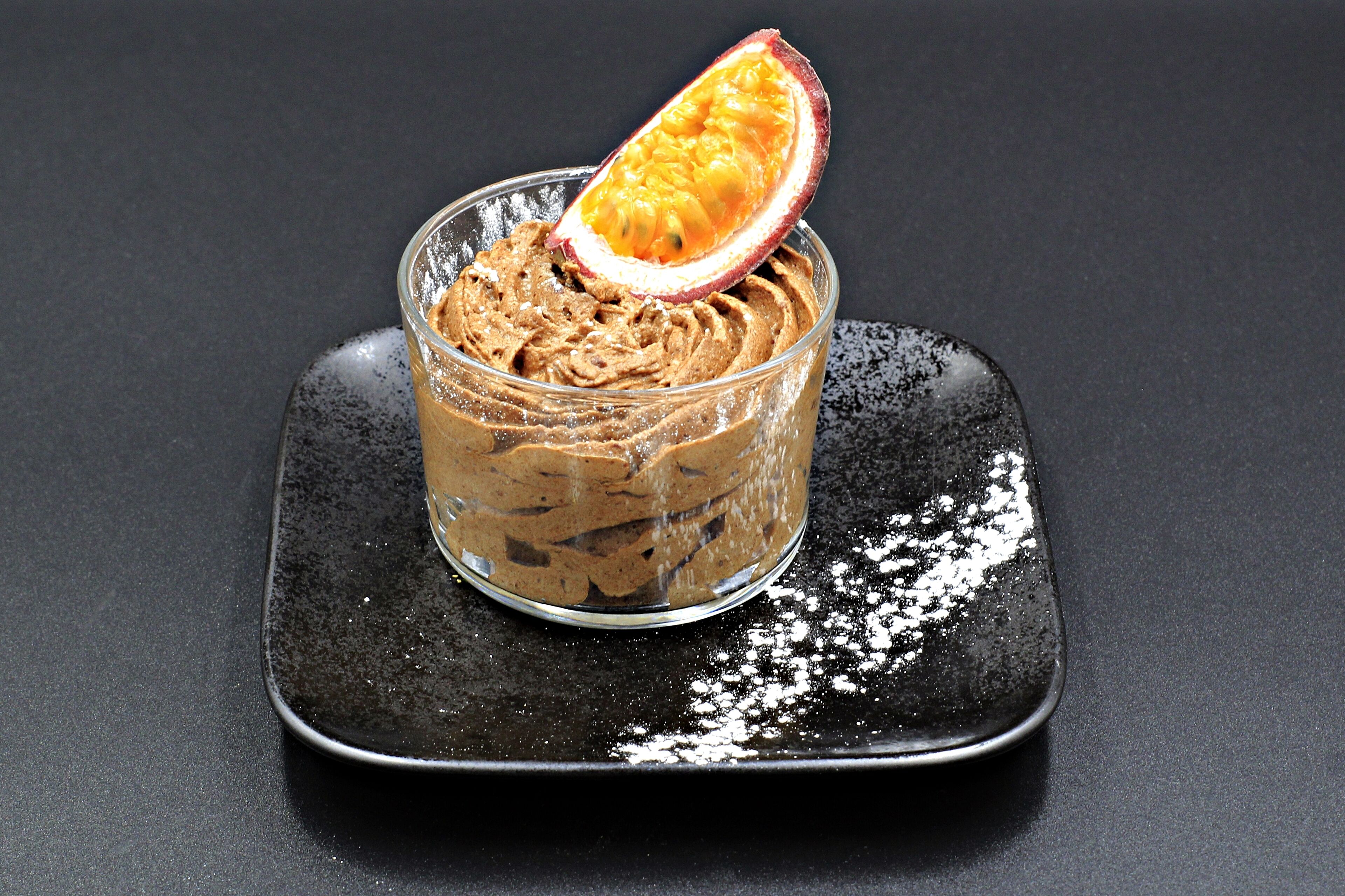 Een dessert in een glas op een zwart bord.
