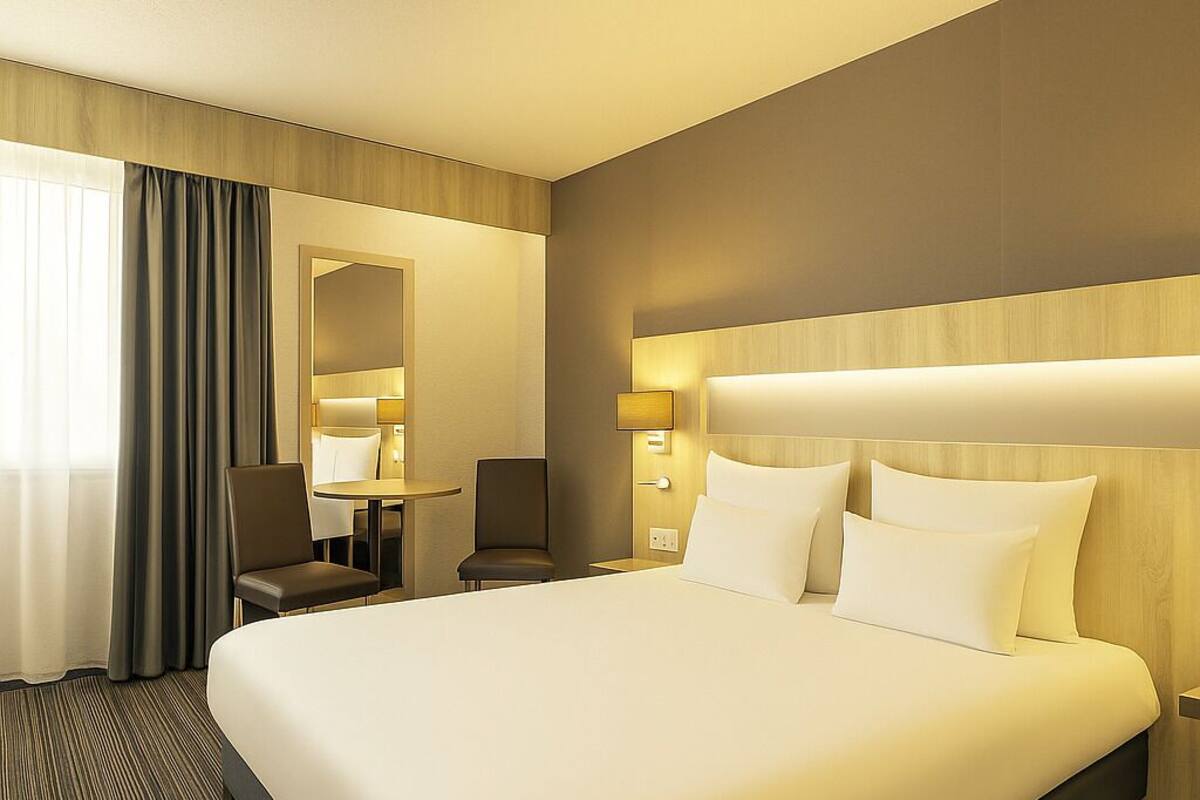 Ein Hotelzimmer mit einem großen Bett, einem Schreibtisch, einem Stuhl und einem Spiegel.