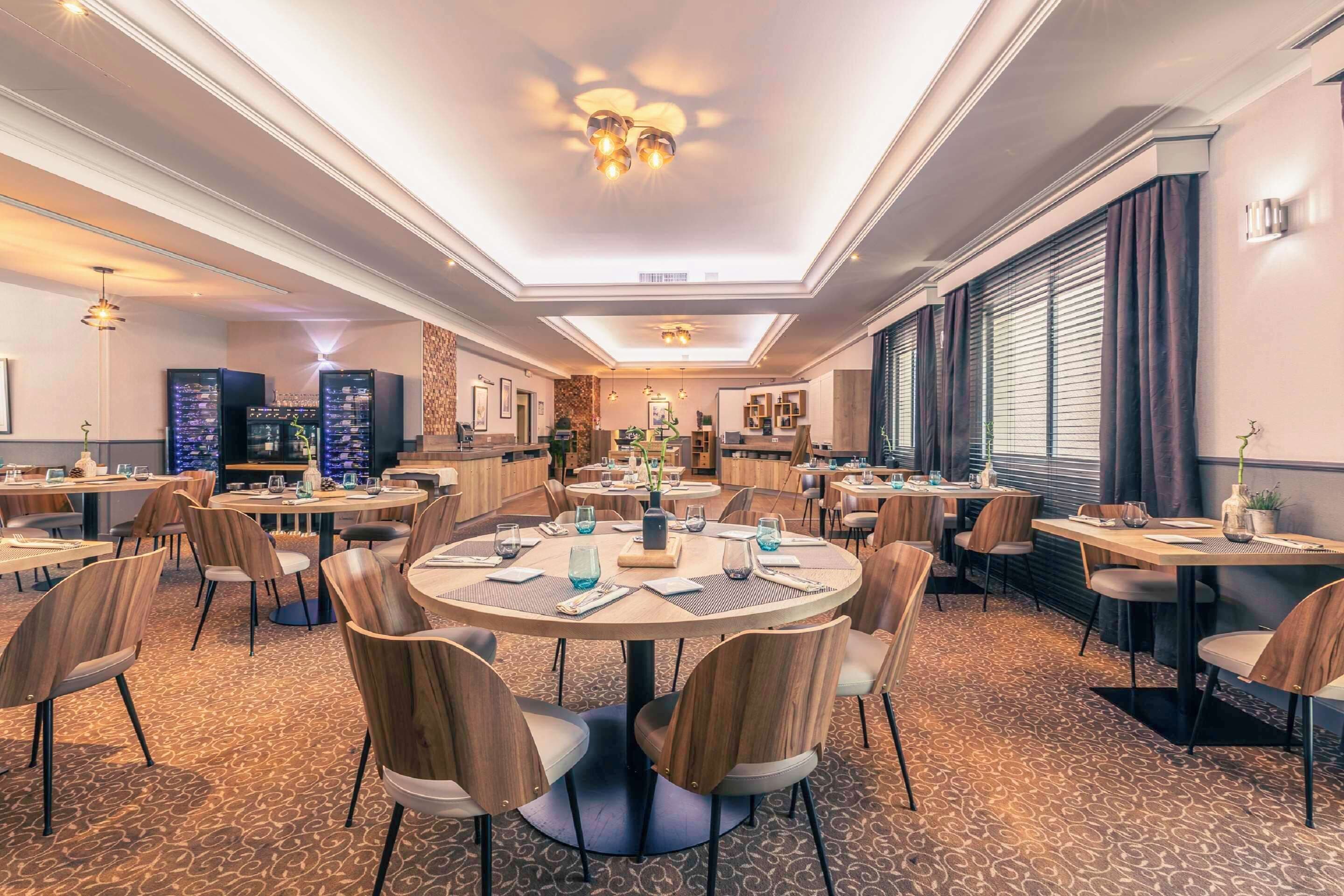 A hotel dining area with round tables, wooden chairs, and a patterned carpet.