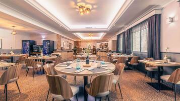 A hotel dining area with round tables, wooden chairs, and a patterned carpet.