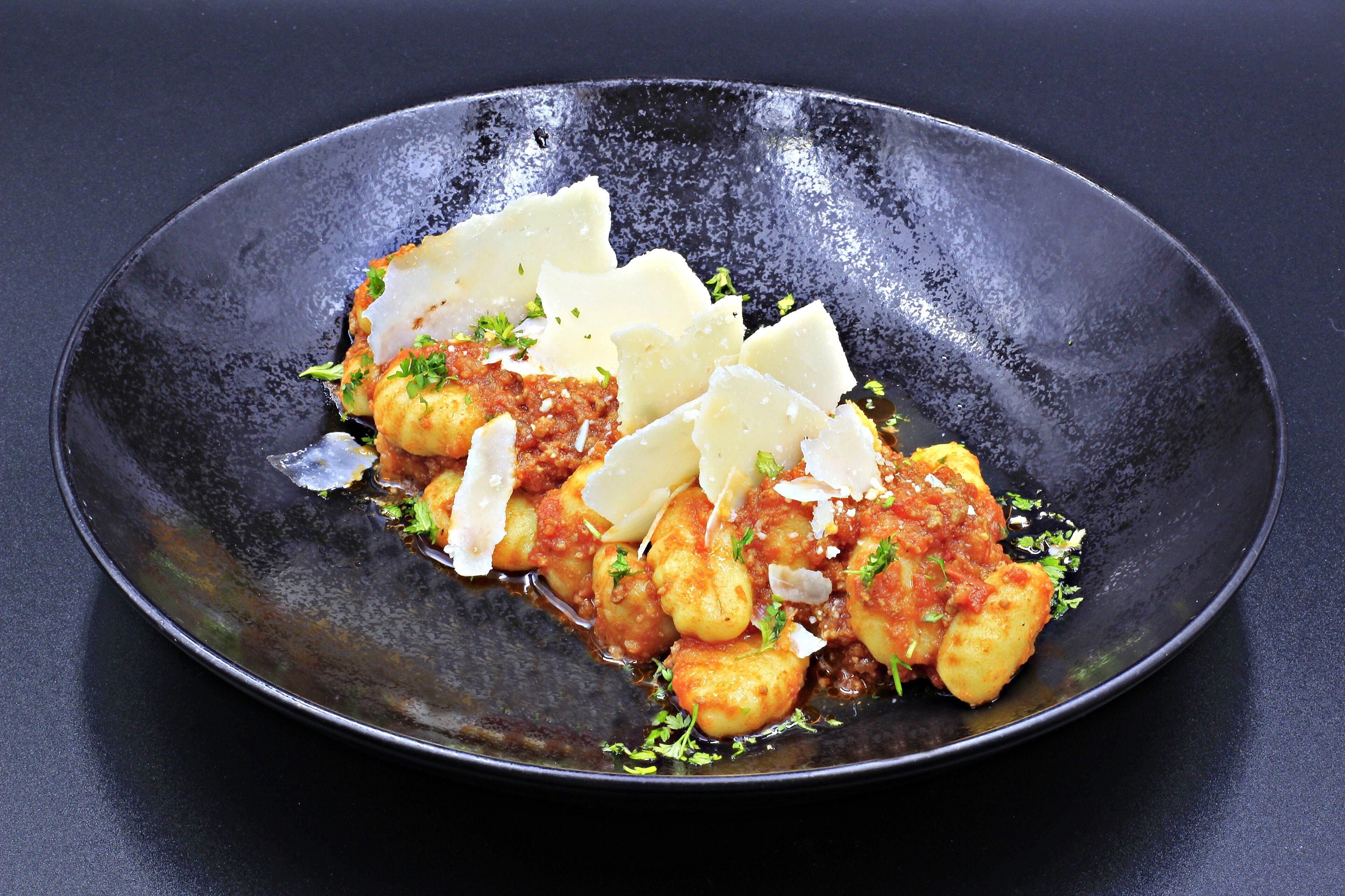 Ein Teller Gnocchi mit Tomatensauce, bestreut mit geriebenem Käse und Kräutern, serviert auf einem schwarzen Teller.