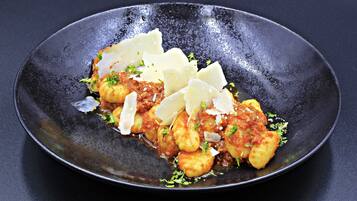 Un plat de gnocchis nappés d’une sauce à base de tomates, garni de fromage râpé et d’herbes, et servi dans une assiette noire.