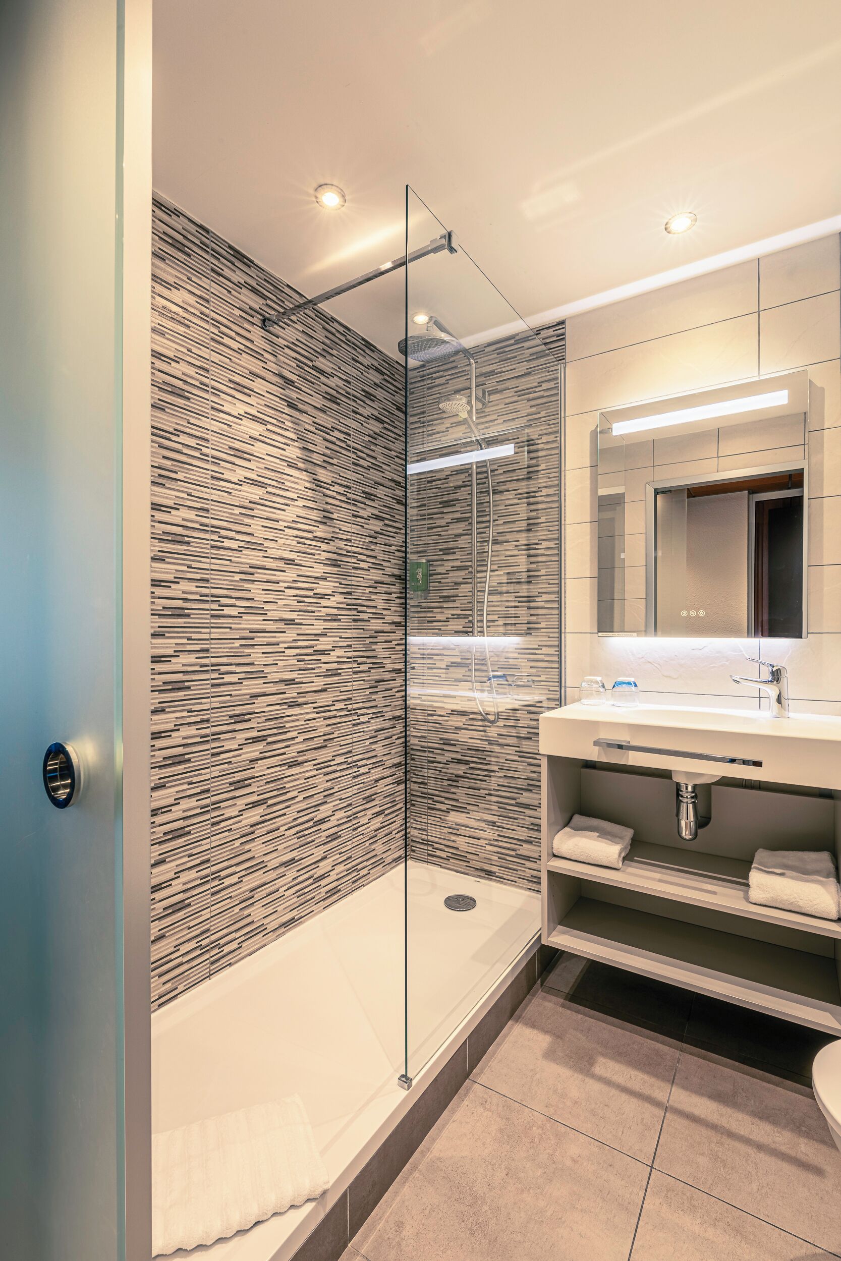 Une salle de bain moderne dotée d’une douche à parois de verre, d’un meuble-lavabo avec miroir et d’un évier encastré.