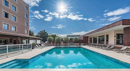 A swimming pool with lounge chairs, a clear sky, and buildings in the background.