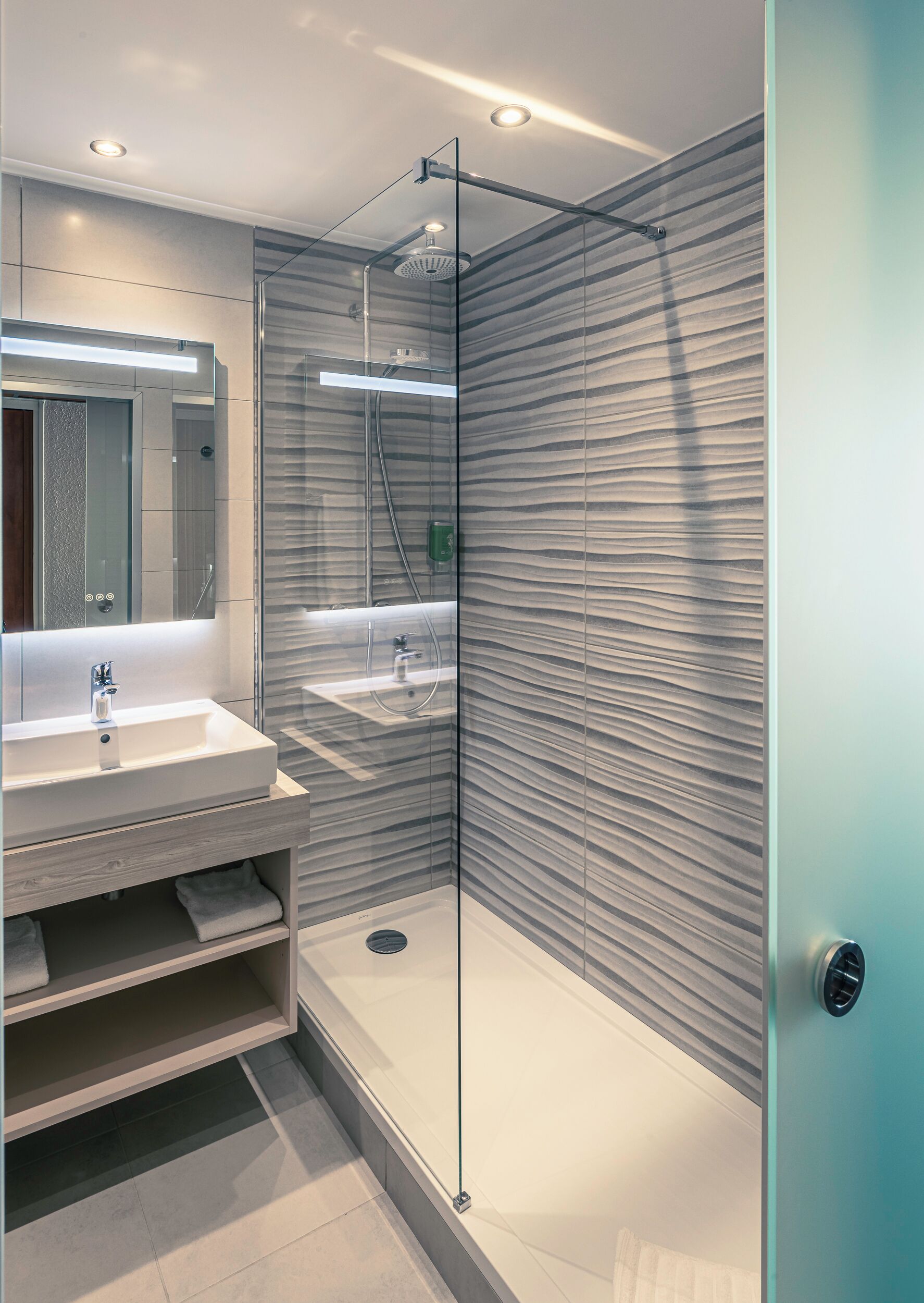 A modern bathroom with a glass-enclosed shower, a vanity with a mirror, and a towel rack.