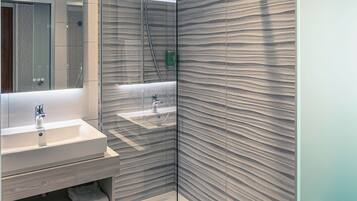 A modern bathroom with a glass-enclosed shower, a vanity with a mirror, and a towel rack.