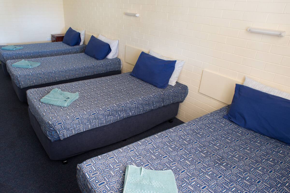 A hotel room with three single beds, each with a patterned duvet cover and pillows.