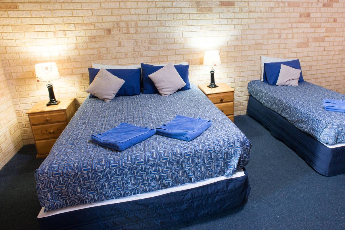 A hotel room with two beds, each with a blue patterned bedspread and pillows. There are two bedside tables with lamps, and the walls are made of brick.
