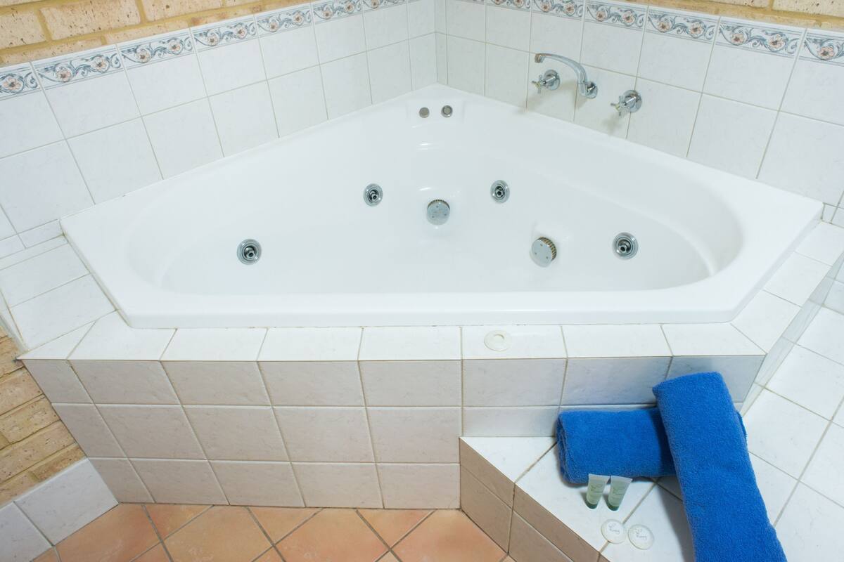 A white bathtub with multiple faucets, a blue towel, and toiletries on a tiled floor.
